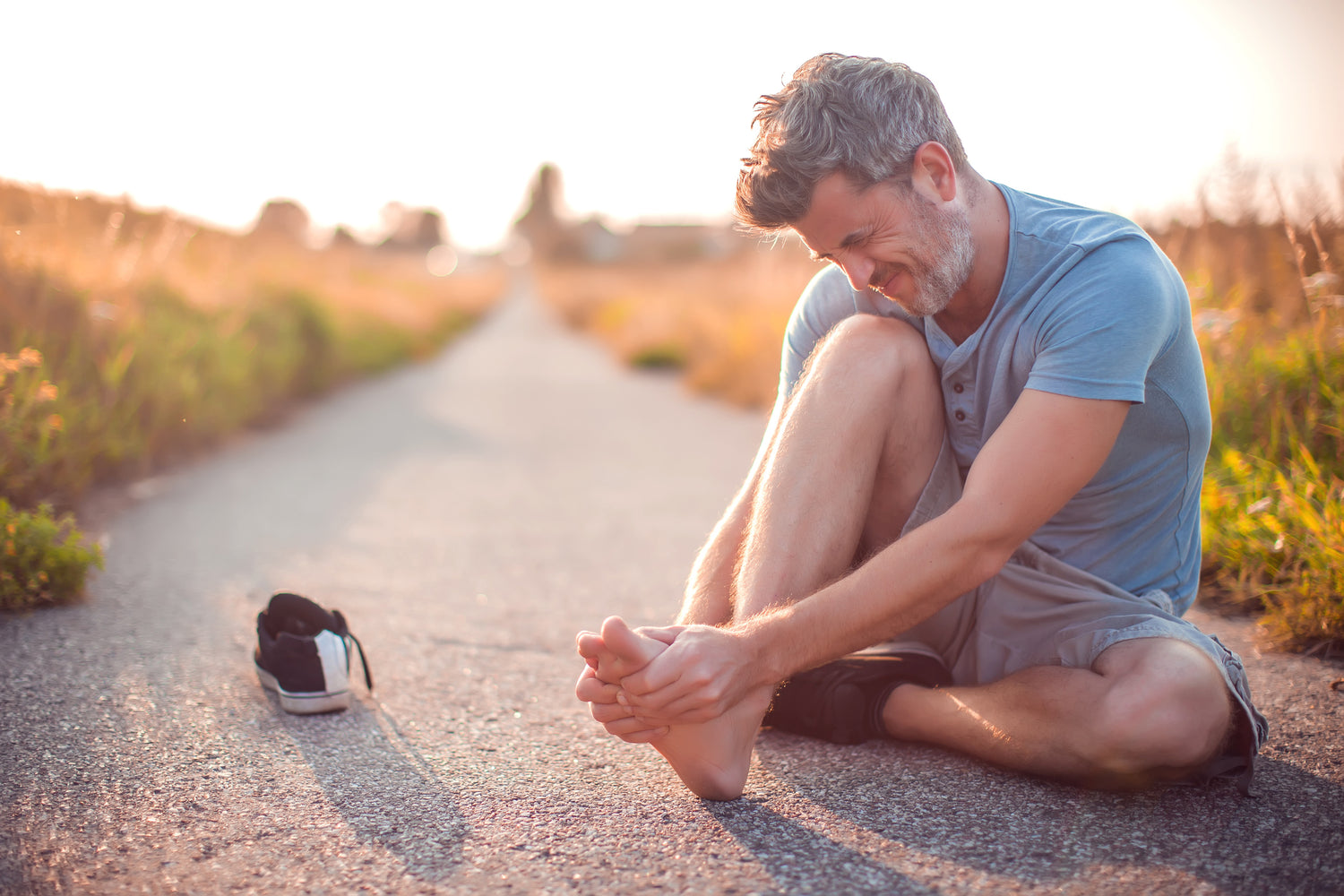 Man sitting on a road with a shoe off, possibly injured, during sunset.