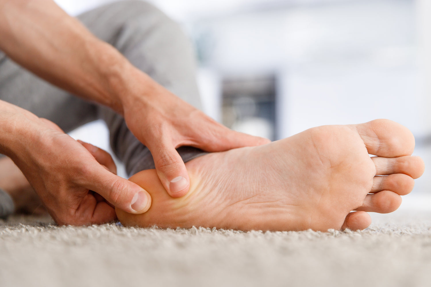 Person massaging foot on a carpeted floor.