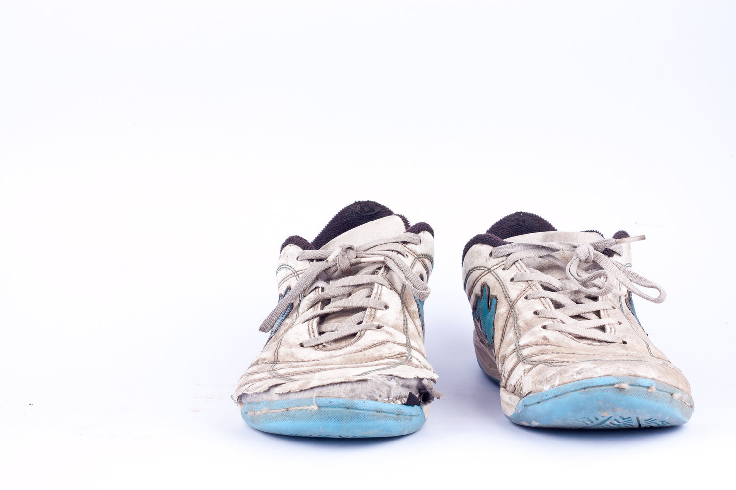 Pair of dirty white sneakers with blue soles on a white background